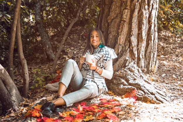 Cheerful female with mug in autumn forest