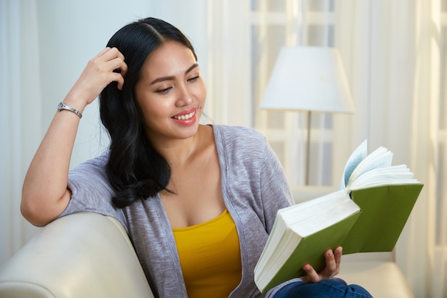 Free photo cheerful filipino woman reading on couch