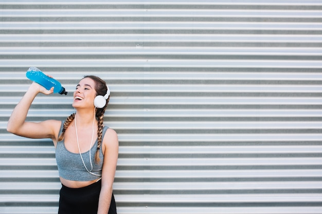 Cheerful fit woman in headphones drinking