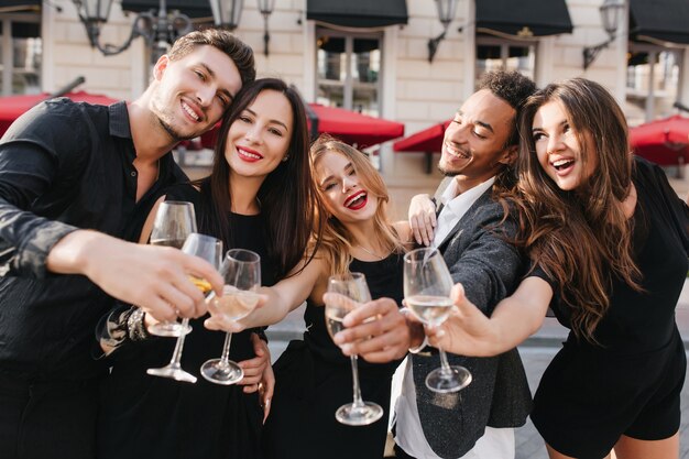 Веселые друзья пьют шампанское на вечеринке на открытом воздухе