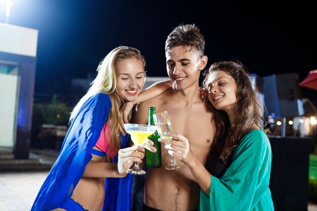 Веселые друзья улыбаются, радуются, отдыхают на вечеринке возле бассейна
