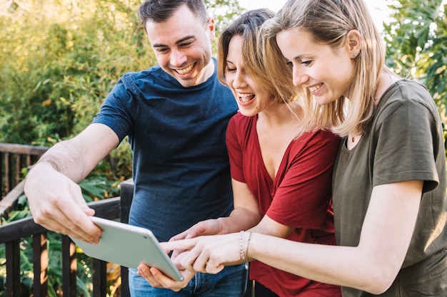 Cheerful friends using tablet near fence