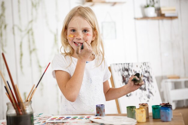 Cheerful and full of joy creative little blonde smiling  and touching her face with dirty hands