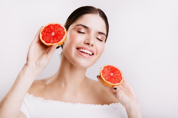 白い壁に笑顔、美味しくておいしい柑橘系の果物を手に持って、素晴らしい気分で陽気な女の子。