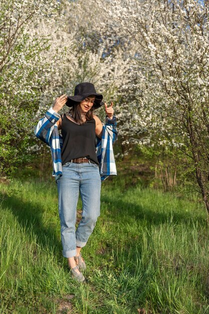春に咲く木々に囲まれた帽子をかぶった陽気な女の子、カジュアルなスタイル。