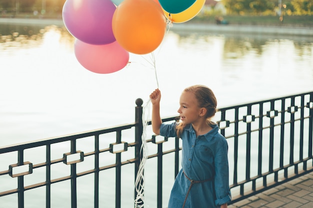 Cheerful girl holding colorful balloons and childish suitcase