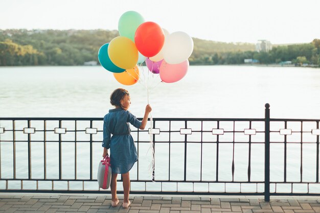 Cheerful girl holding colorful balloons and childish suitcase