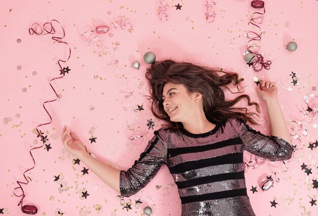 Cheerful girl lies on a pink background among confetti and serpentine top view