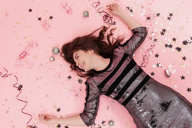 Cheerful girl lies on a pink background among confetti and serpentine top view