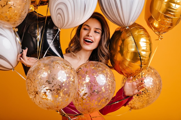 Cheerful girl preparing for party Merry female model holding sparkle balloons