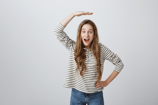 Cheerful girl raising hand up above head and look amazed, showing growth
