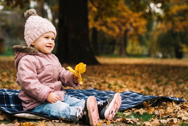 Cheerful girl sitting on underlay in autumn forest
