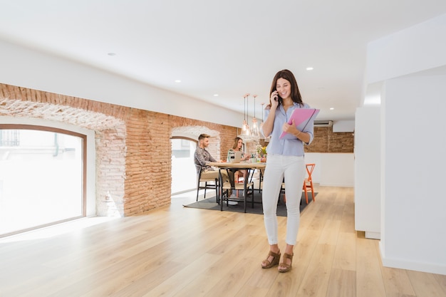 Cheerful girl talking phone in modern office