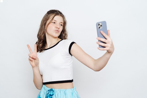 Cheerful Girl teenager taking selfie with phone while posing on white