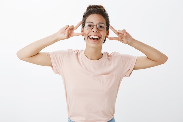 Cheerful girl with glasses posing against the white wall