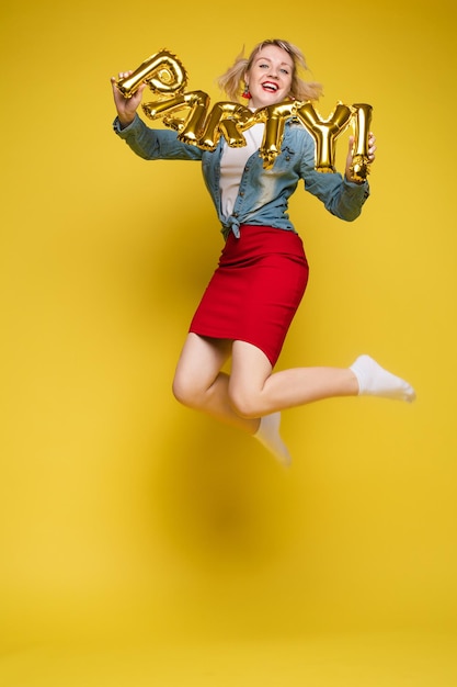 Cheerful girl with inflatable letters HAPPYStock photo portrait of attractive girl with red lips holding shining bright inflatable word HAPPY Isolate on orange background