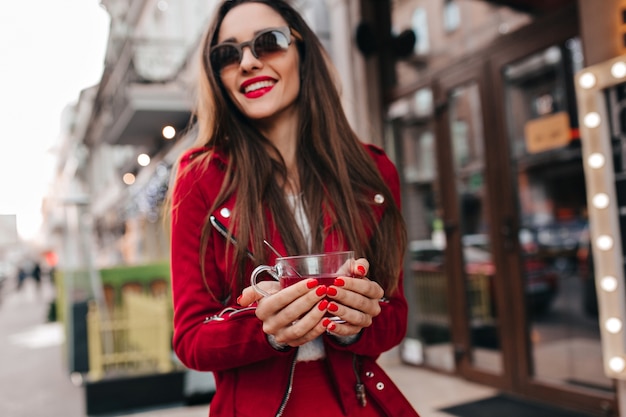 Ragazza allegra con il manicure rosso che tiene tazza di tè