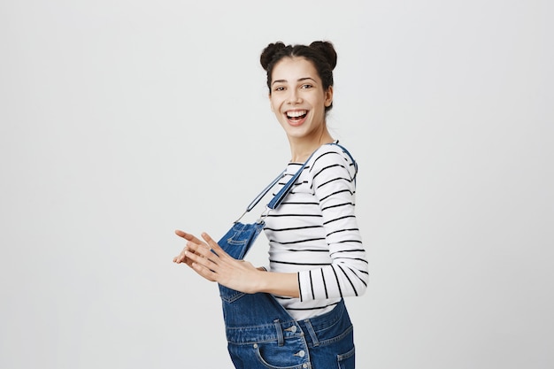 Cheerful good-looking brunette girl with buns hairstyle, wearing overalls and feeling confident