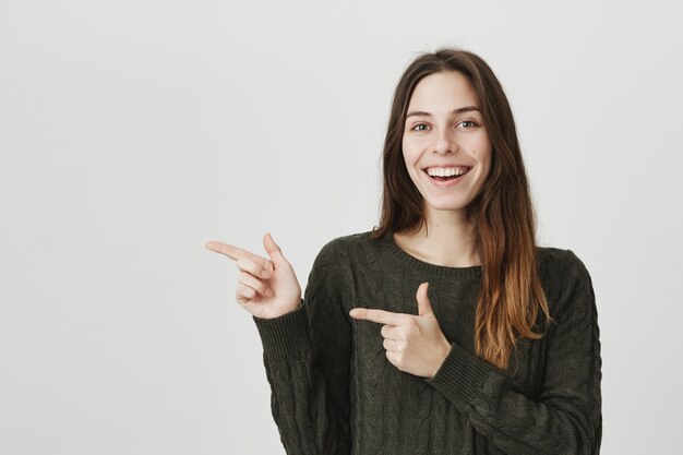 Cheerful good-looking woman pointing fingers left, inviting