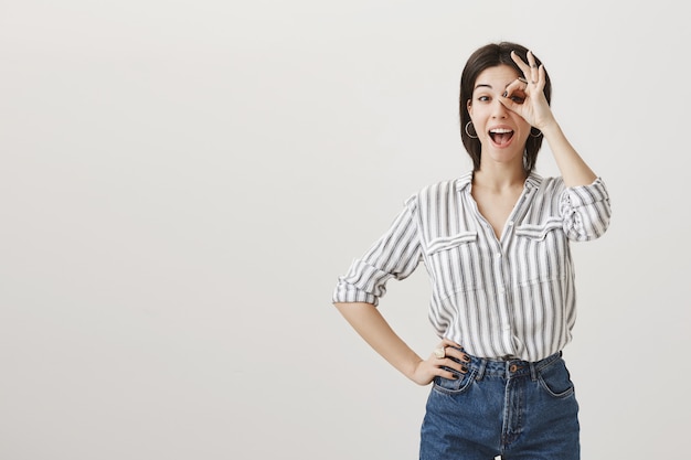 Cheerful gorgeous woman showing okay gesture on eye and smiling assertive