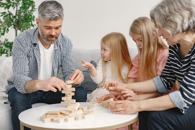 Cheerful grandparents and grandchildren playing blocks wood tower game together. living room interior.