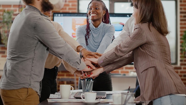 Cheerful group of workmates celebrating business success in startup office. People feeling happy and satisfied about teamwork achievement, putting hands together in unity. Successful win