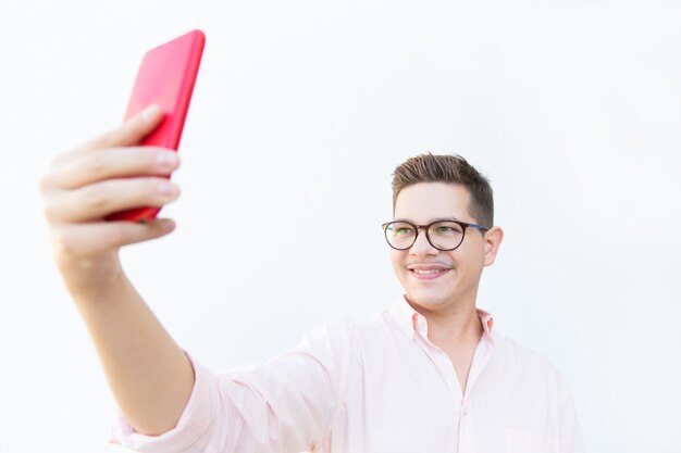 Cheerful guy in eyeglasses holding red mobile phone