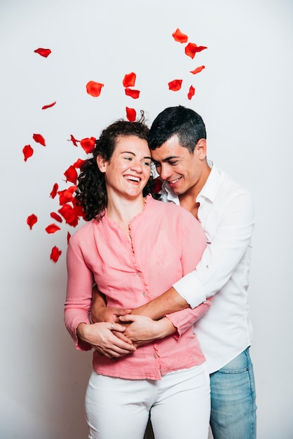 Cheerful guy hugging smiling lady between tossing petals 
