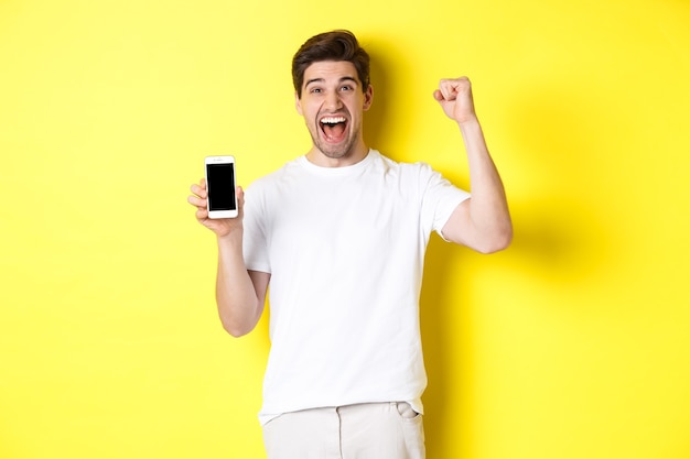 Cheerful guy showing smartphone screen, raising hand up and celebrating, triumphing over internet