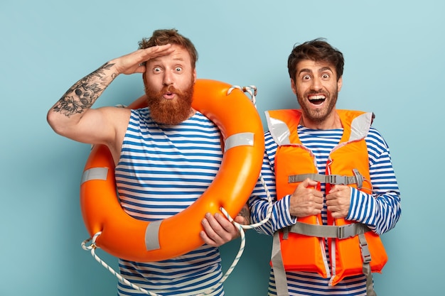 Free photo cheerful guys posing at the beach with lifejacket and lifebuoy