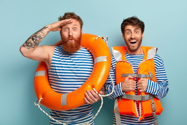 Cheerful guys posing at the beach with lifejacket and lifebuoy