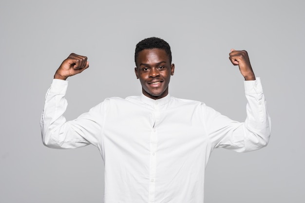 Cheerful handsome African guy in short white shirt making yes gesture while excited about winning. Ecstatic young fan rooting and expressing support.