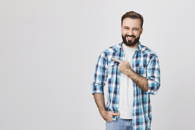 Cheerful handsome bearded man pointing upper left corner and smiling