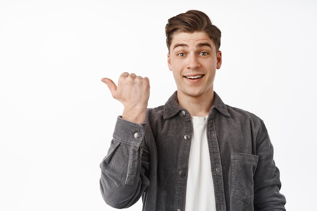 Cheerful handsome guy pointing left, student showing discount in store, recommending click on link, visit shop, try this product, standing against white background