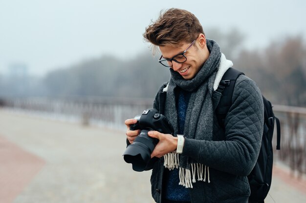 Cheerful handsome man in eyeglasses looks at photos in the camera.