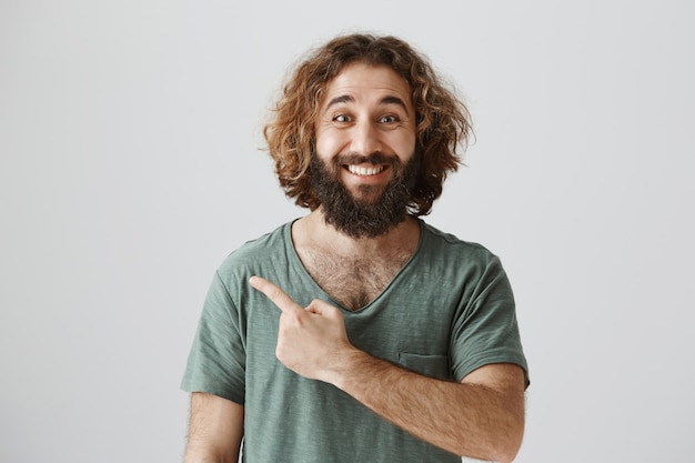 Free photo cheerful handsome middle-eastern guy pointing finger at advertisement