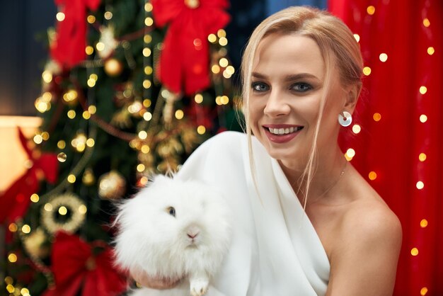白い毛むくじゃらのウサギを保持している陽気な幸せな女性
