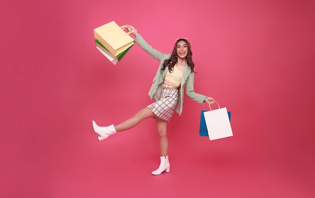 Free photo cheerful happy thai asian woman enjoying shopping she is carrying shopping bags get the latest offers at the shopping center isolated on pink studio background