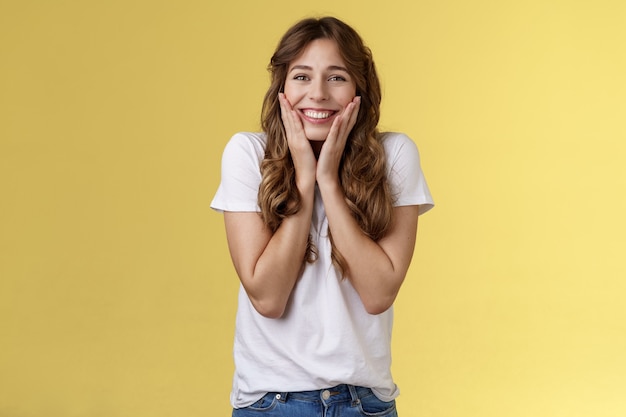 Allegra felice ottimista giovane ragazza riceve un'incredibile opportunità di studio all'estero studente tifo celebrando notizie sbalorditive toccare le guance arrossendo gioia felicità sorridente ampiamente sfondo giallo.