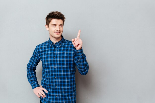 Cheerful happy young man standing over grey wall and pointing