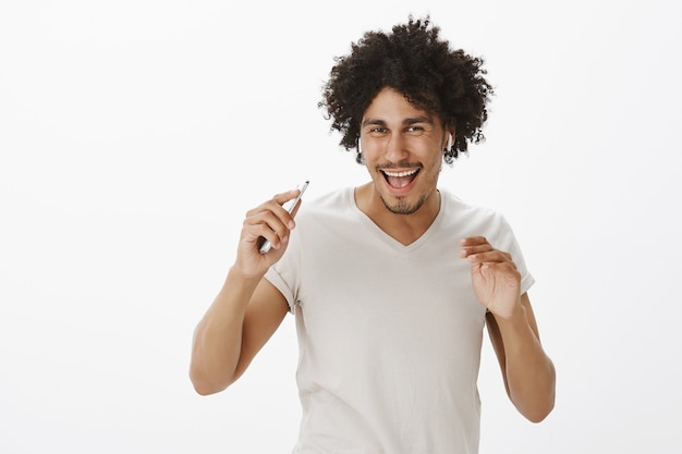 Cheerful hipster man in wireless earphones, dancing and listening music on smartphone