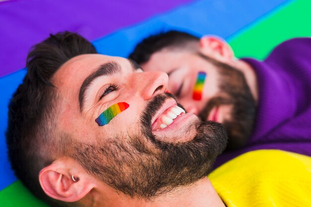 Cheerful homosexual with partner on rainbow flag
