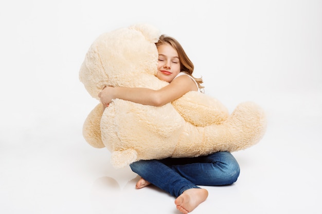 Cheerful kid sitting on floor holding toy bear on knees.