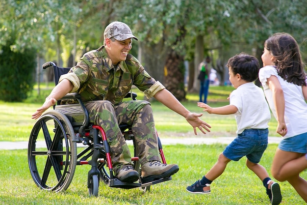 陽気な子供たちは軍のお父さんに会い、抱擁のために両手を広げてカモフラージュで障害者の男に走っています。戦争のベテランまたは帰国の概念