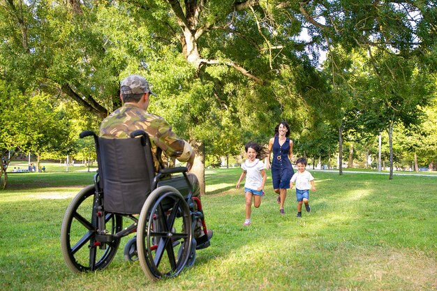 陽気な子供たちとその母親が軍の父に会い、カモフラージュで障害者の男に走っています。戦争のベテランまたは帰国の概念