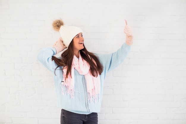 Cheerful lady in mittens, bobble hat and scarf taking selfie on smartphone