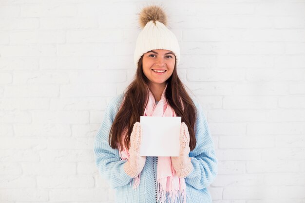 Cheerful lady in mittens, bobble hat and scarf with square paper 