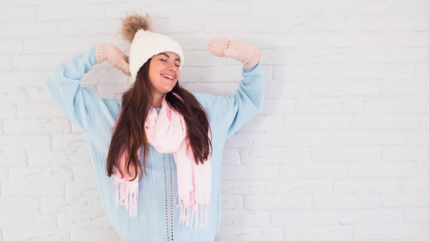 Cheerful lady in mittens, bobble hat and scarf with upping hands 