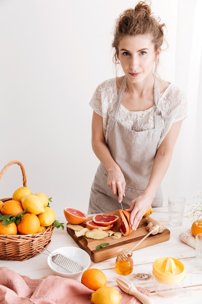 Cheerful lady standing near table with a lot of citruses