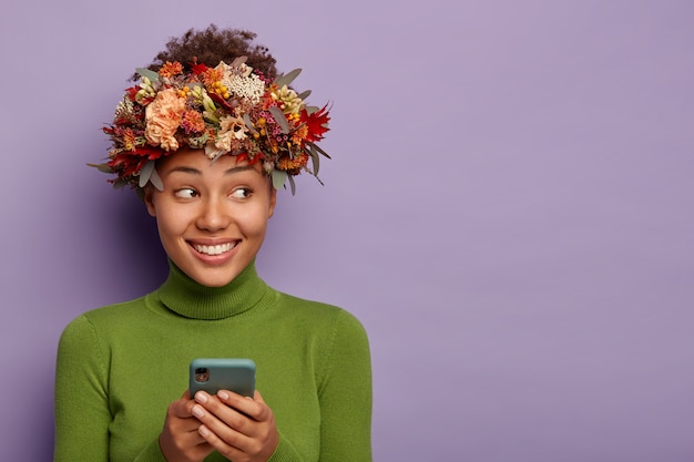 黒い肌、歯を見せる笑顔、秋の植物の美しい花輪、携帯電話からのメッセージ、嬉しい表情で脇に見える陽気な女性